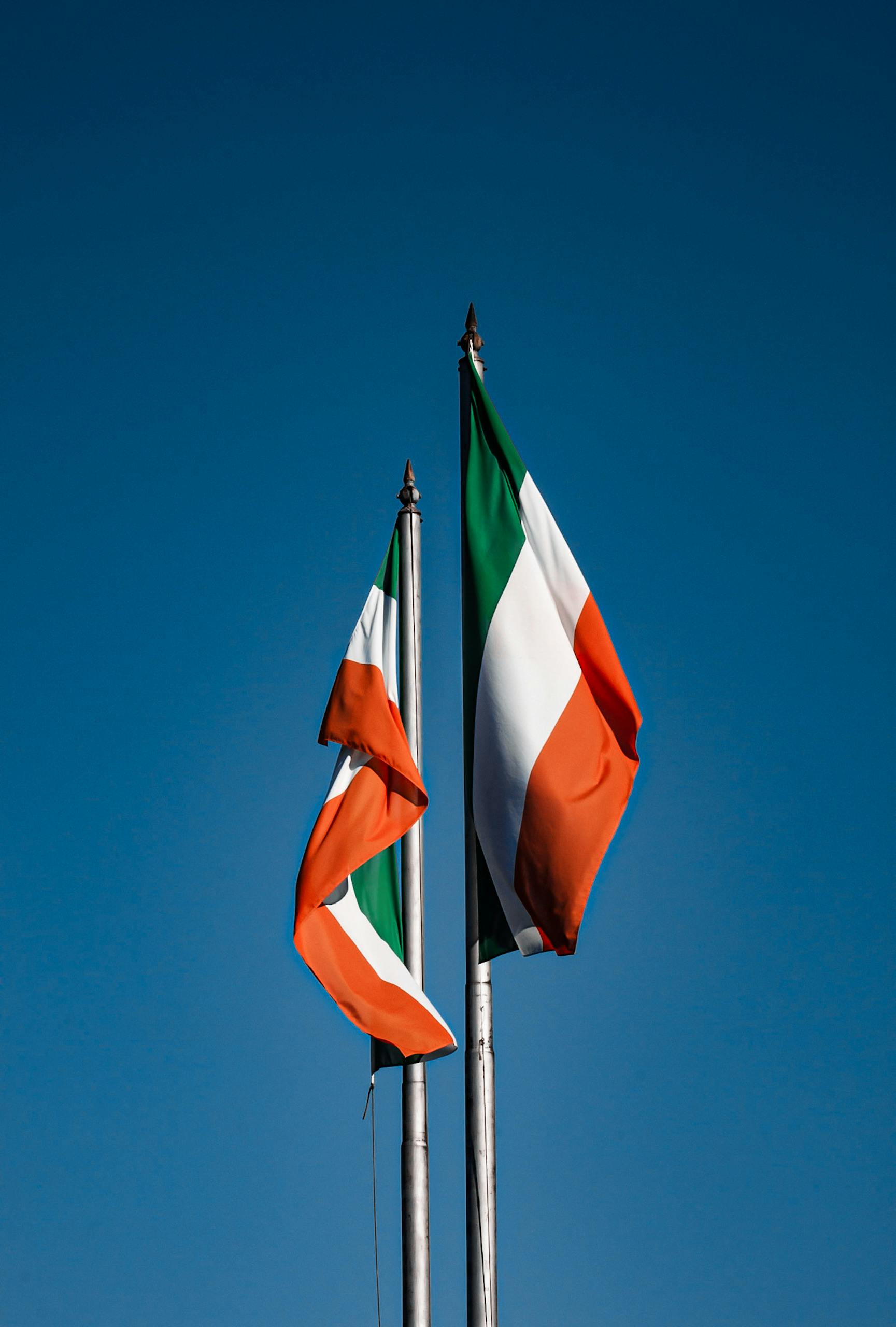 Vibrant Irish flags waving on flagpoles set against a clear blue sky in Dublin, Ireland.